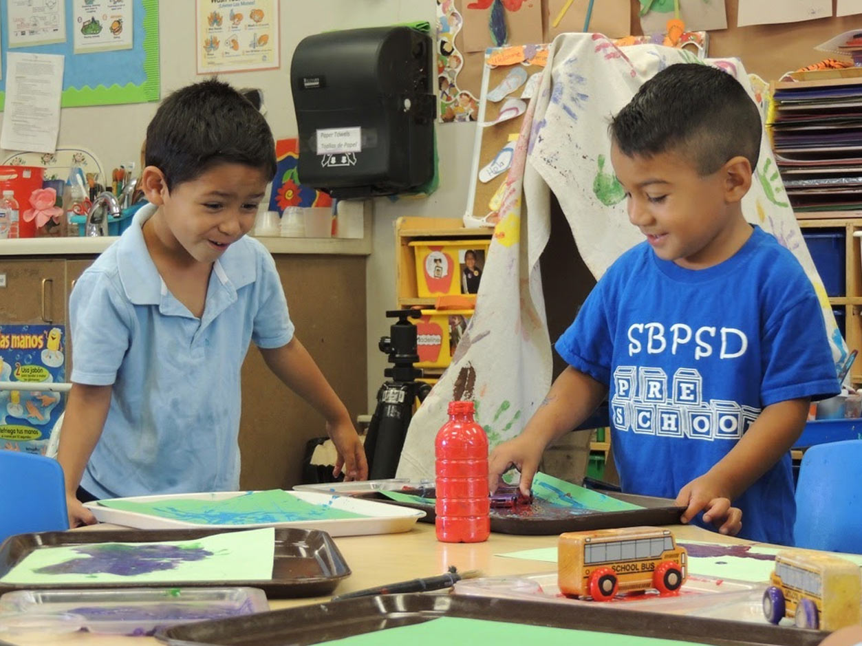 an image of two boys working with art supplies at a desk in a classroom