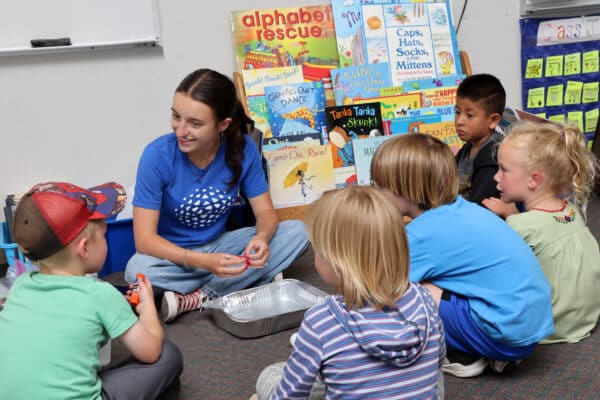A teacher sits in a circle with students, preparing for a science experiment
